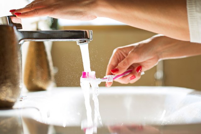 A close-up image of a women holding a toothbrush under a facet