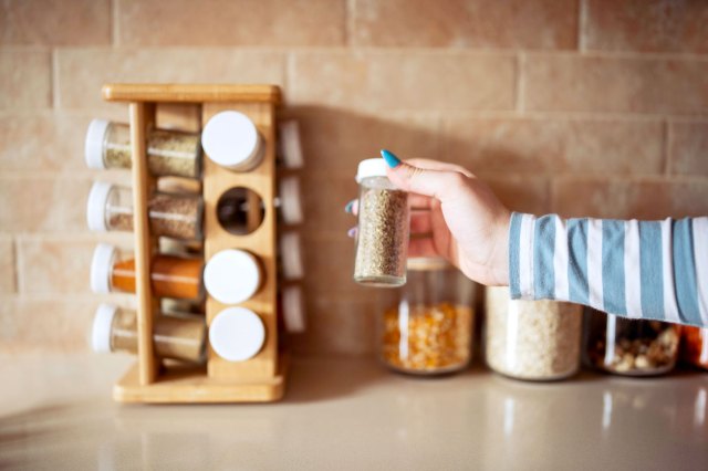 An image of a person wearing a blue and white shirt taking a spice jar off of a spice rack