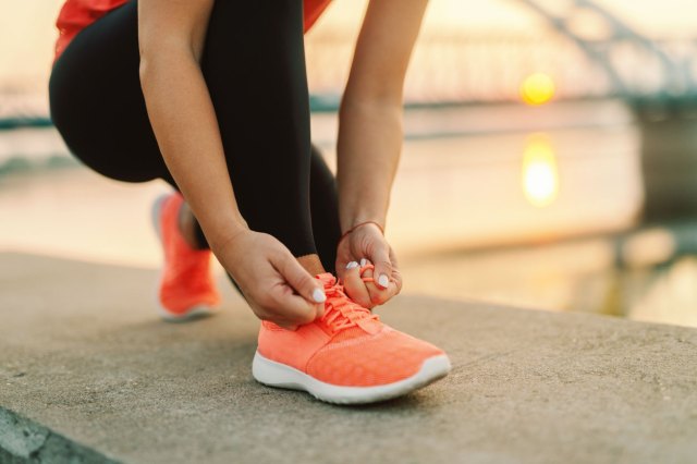 A close-up image of a woman bending down to tie her sneaker