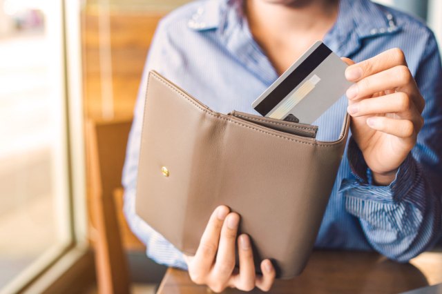 A person pulls a credit card out of a tan wallet