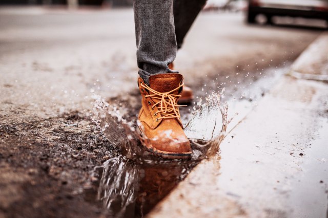 A person wearing a pair of brown boots splashes in a puddle