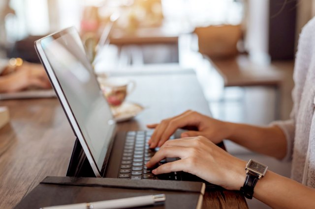 A person wearing a black watch types on a laptop keyboard