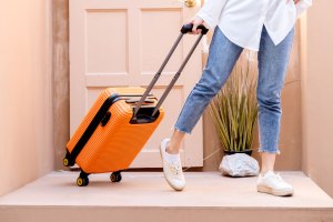 Woman in jeans pulls an orange suitcase on a doorstop.