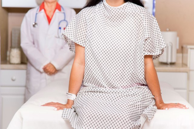 An image of a woman in a hospital gown sitting on examining table