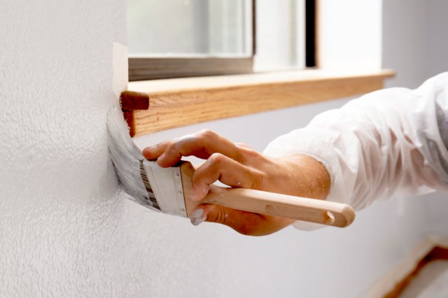 An image of a person painting a white wall around a window