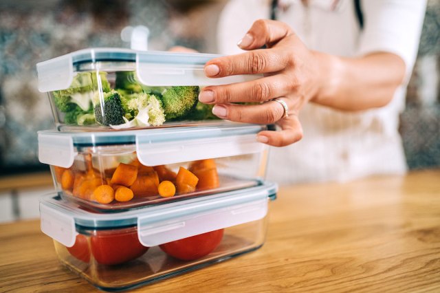 A woman stacks clear glass containers filled with food on a wooden surface