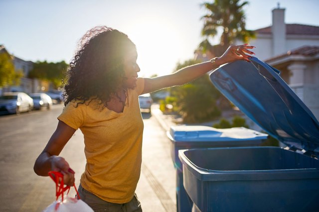 An image of a woman opening a blue recycling bin