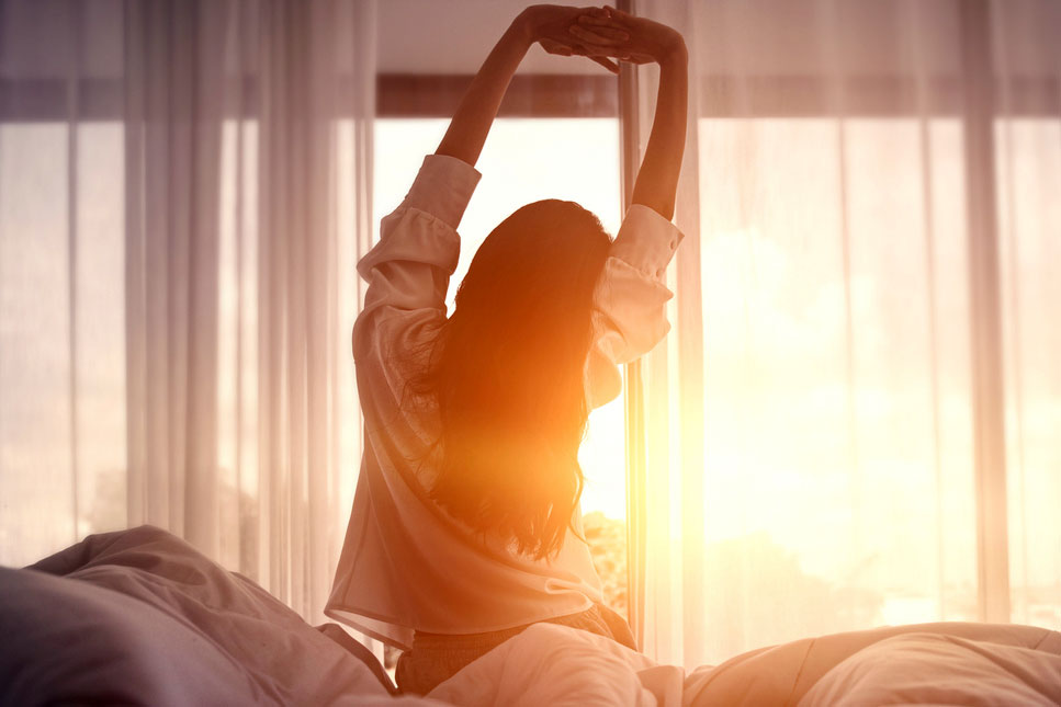 An image of a woman stretching in bed at sunrise