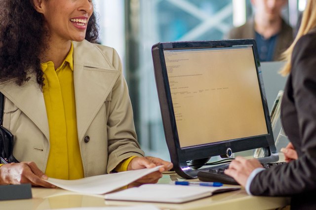 An image of a woman holding a document and smiling while bank teller serving.