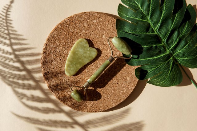 An image of a jade roller and a gua sha tool on a cork plate