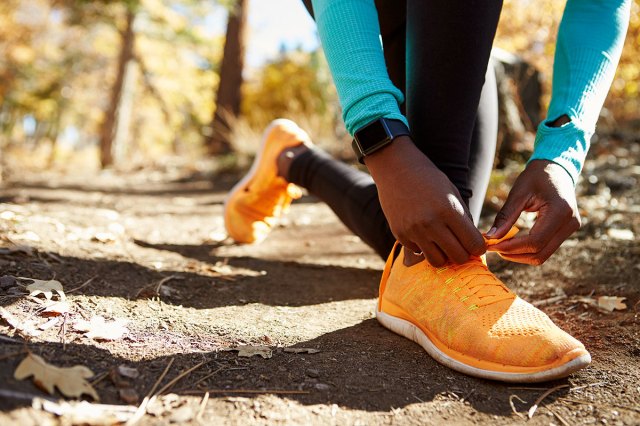 An image of a person kneeling on the ground and tying their sneaker