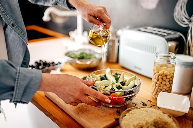 An image of a person pouring oil into a bowl of vegetables