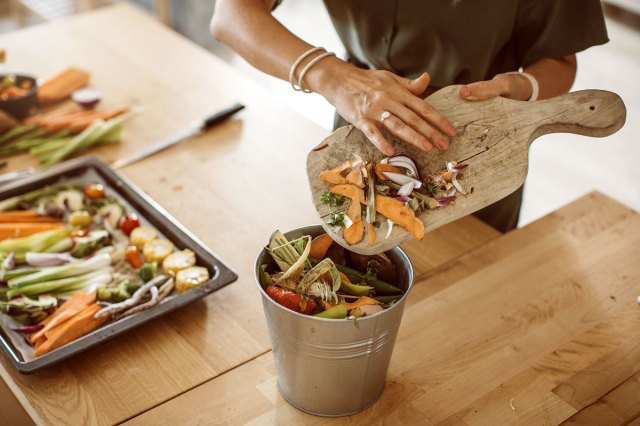 An image of a person pushing food scraps off a cutting board into a compost bucket