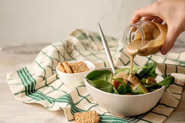 An image of a hand pouring dressing onto a bowl of salad