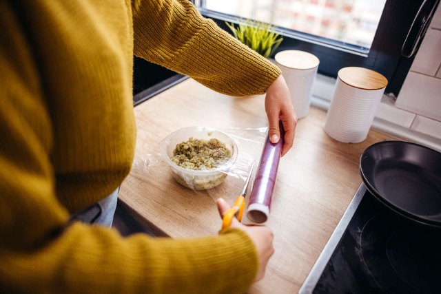 An image of a woman putting plastic wrap over a container of food