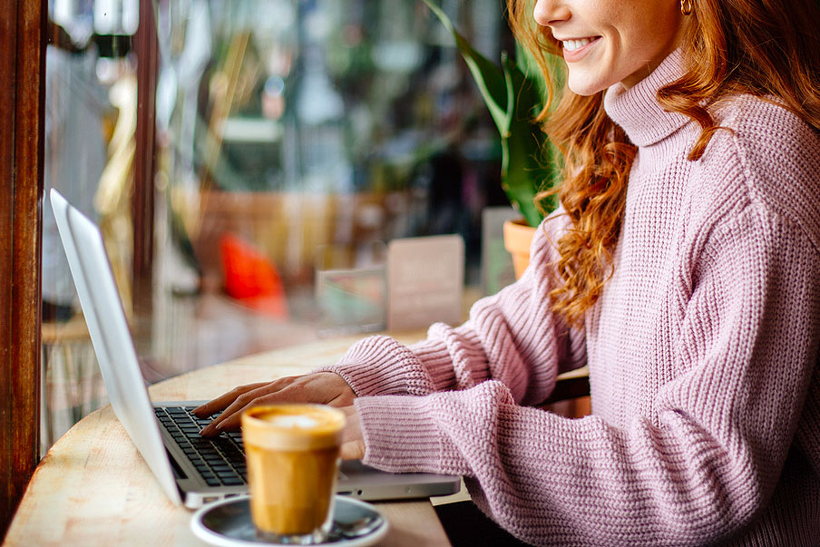 An image of a woman typing on her laptop at a coffee shop