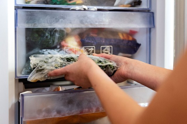 An image of a person putting a bag of vegetables in the freezer