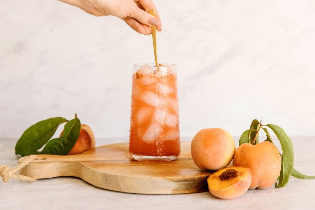 An image of a hand mixing an orange drink on a wooden cutting board