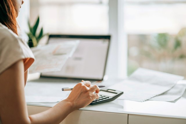 An image of a woman sitting at a desk and typing on a calculator