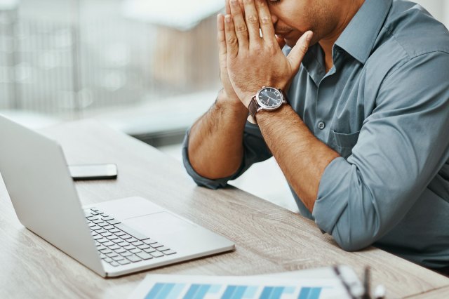 An image of a man with his head in his hands looking at a computer