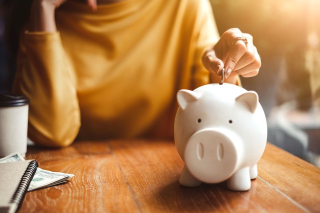 An image of a person putting a coin into a white piggy bank