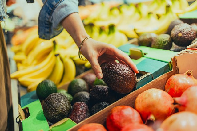 An image of a person grabbing an avocado from the produce section