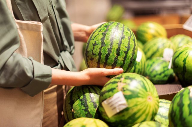 An image of a woman pulling a watermelon from the produce section