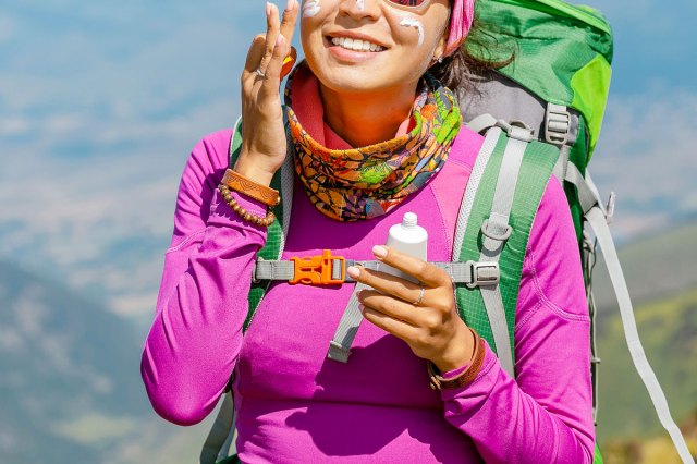 An image of a woman on a hike putting on sunscreen on her face