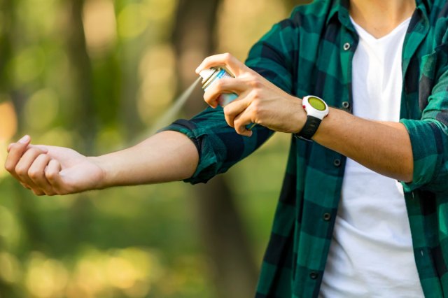 An image of a man spraying bug spray on his arm