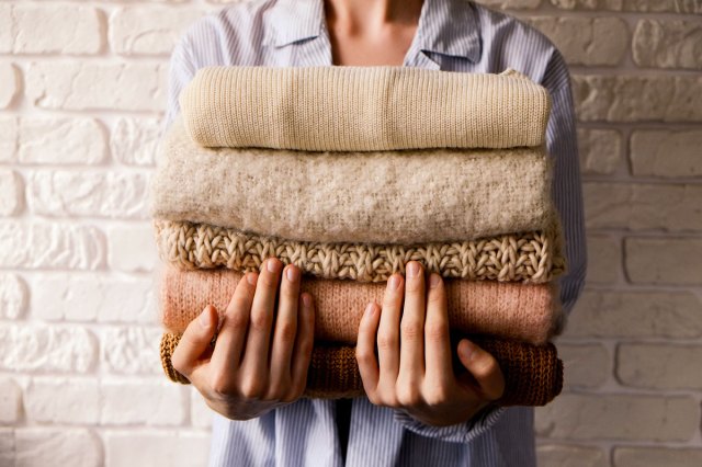 An image of a person holding a pile of folded sweaters