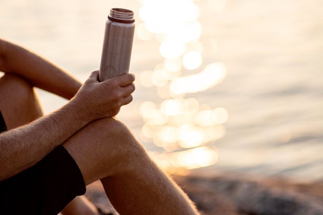 An image of a person holding silver tube near body of water during daytime