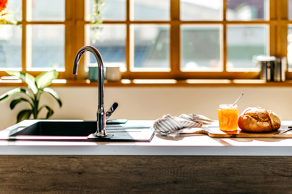 An image of kitchen counter with a sink and a cutting board with jam and a loaf of bread