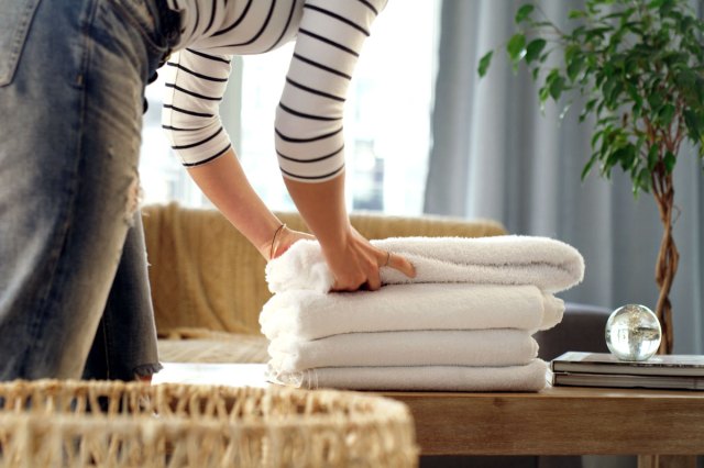 An image of a woman placing a white folded towel on a stack of white folded towels