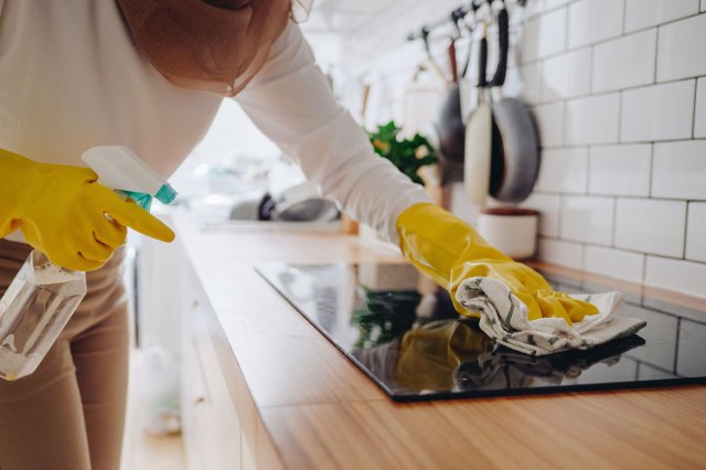 An image of a woman cleaning top top of an oven