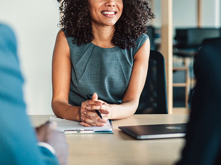 An image of a woman sitting at a desk talking to two people