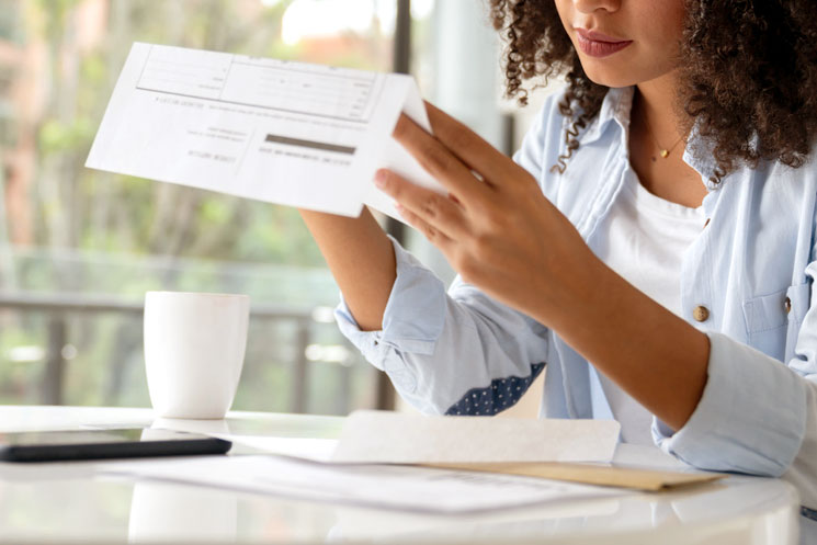 An image of a woman sitting at a table and looking at a bill