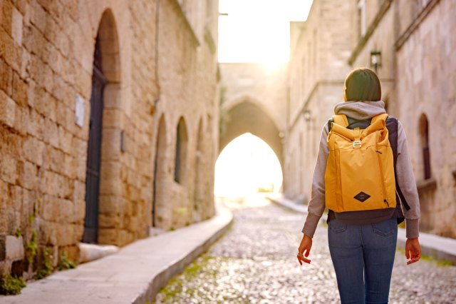 An image of a woman wearing a backpack walking on a cobblestone street