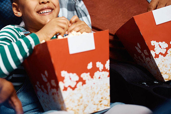 An image of a child holding a big tub of popcorn at the movie theater