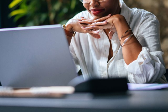 An image of a woman resting her head on her hands while looking at a computer