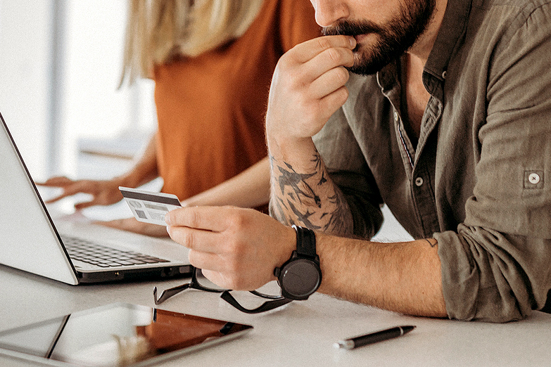 An image of a man looking at his credit card next to a woman on a laptop