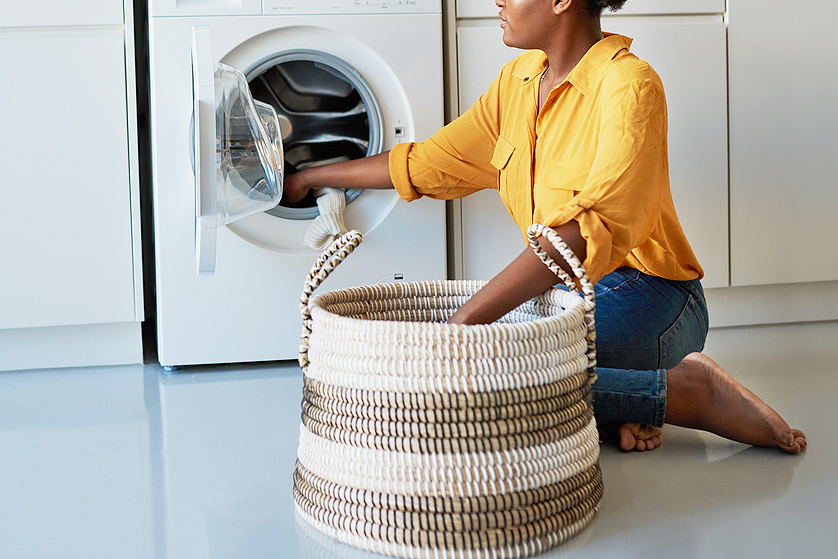 An image of a woman with a basket sitting on the floor taking clothes out of the dryer