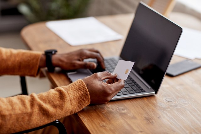 An image of a person on a laptop and holding a credit card