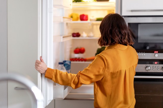 An image of a woman in an orange shirt looking in the fridge