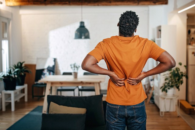 An image of a man in an orange shirt holding his lower back