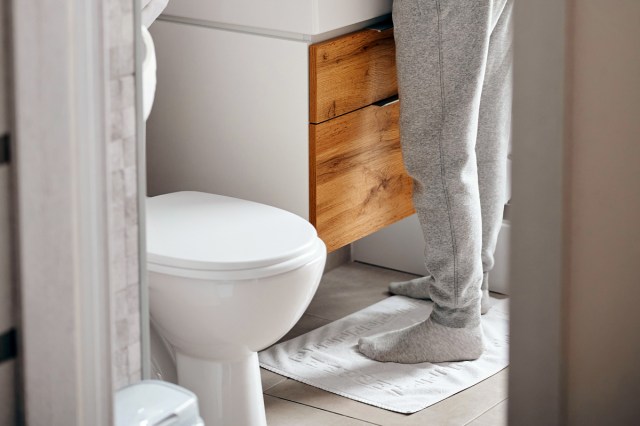 An image of a person standing by a white toilet