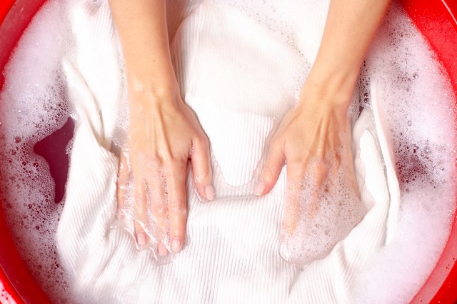 An image of a person washing a white sweater in a red basin