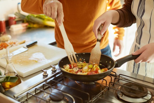 An image of two people stirring food in an skillet