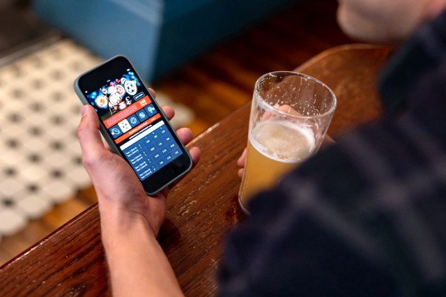 An image of a person holding a phone in one hand and a beer in the other