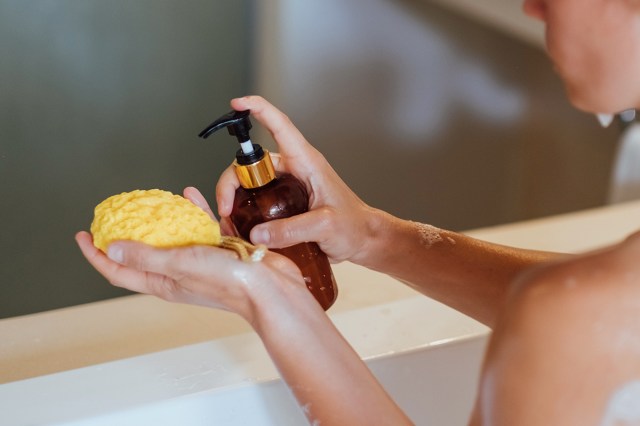 An image of a woman in a bathtub squirting soap onto a yellow sponge