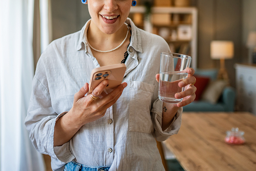 An image of a woman holding a glass of water and her cell phone